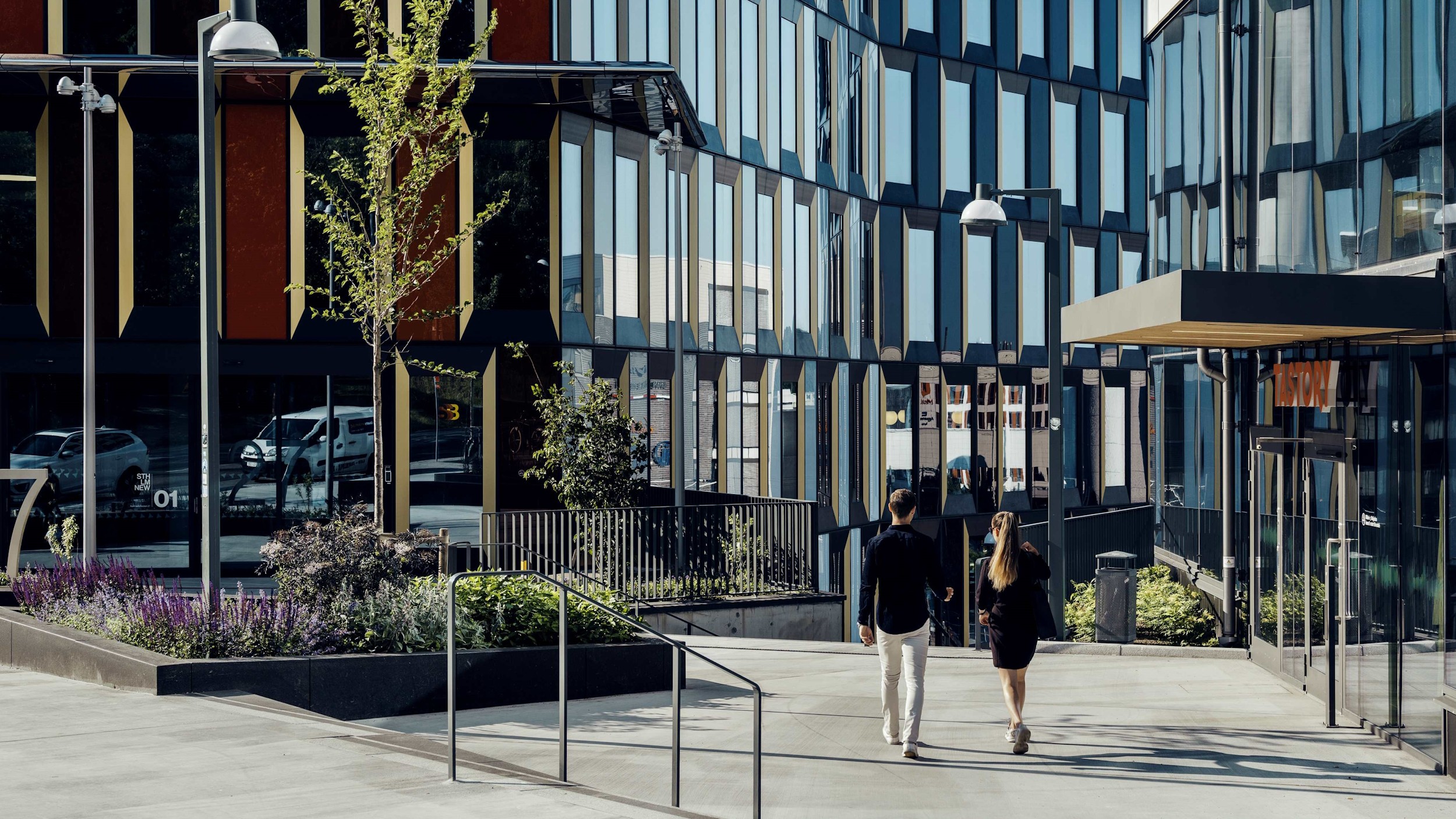 Modern Urban Office Building with People Walking Modern office complex exterior with two people walking on a sunny pathway amidst glass buildings.