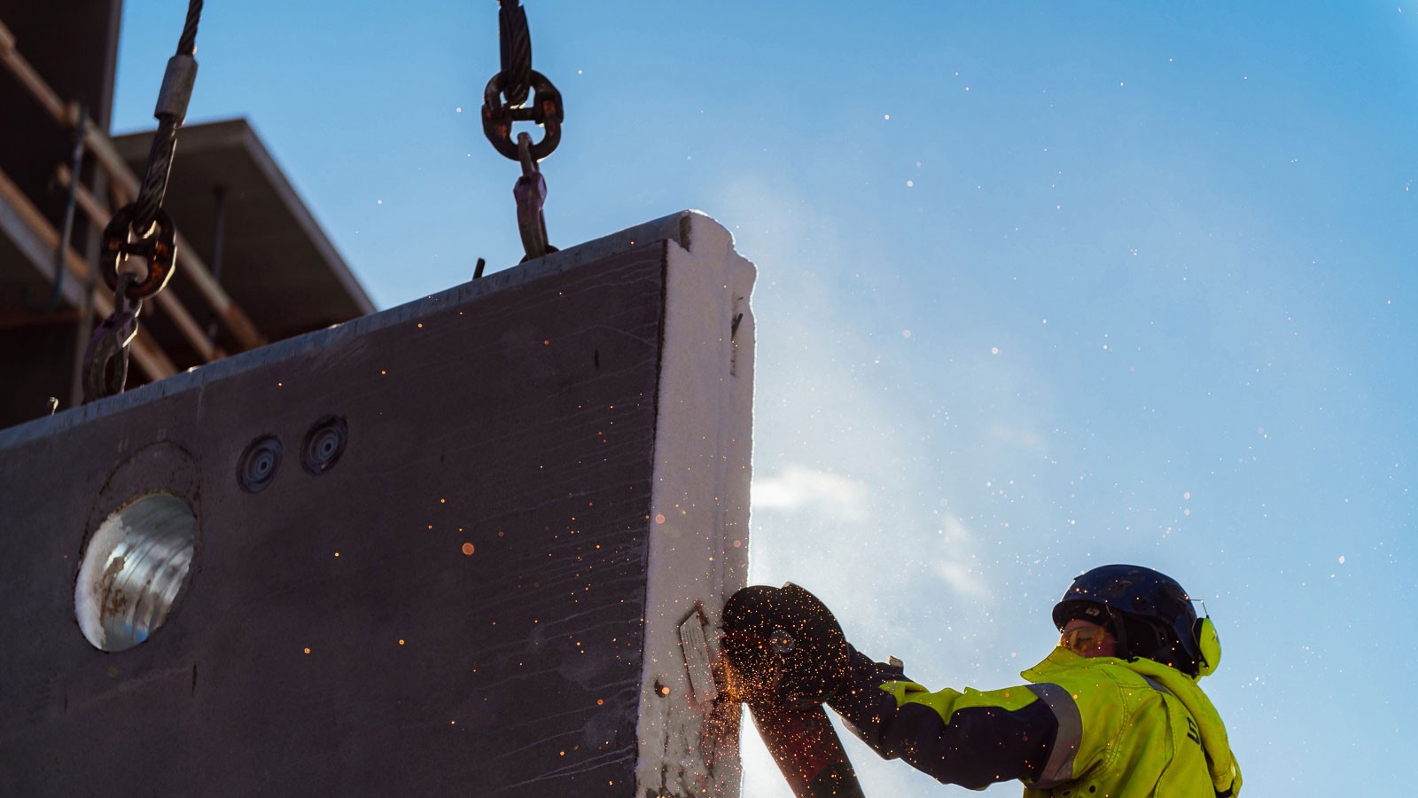 Construction worker cutting a suspended concrete slab with a saw, producing sparks.