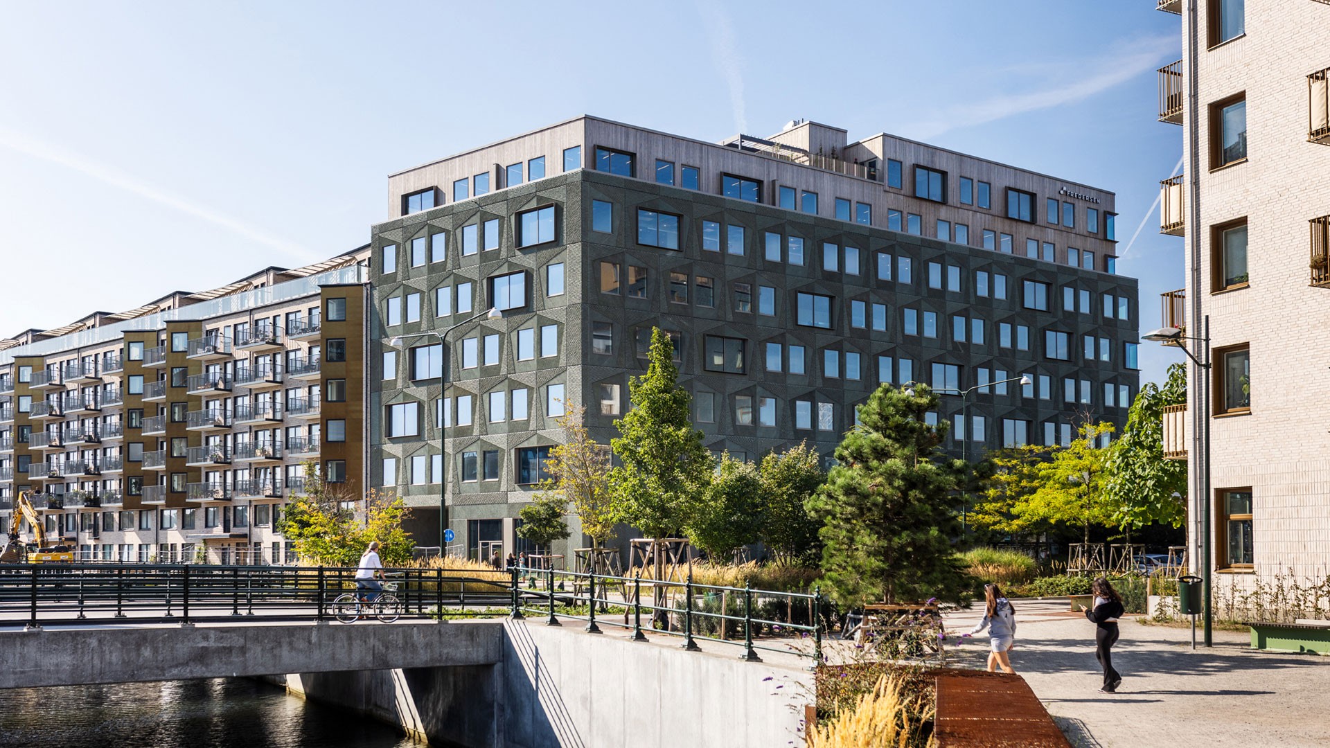 Modern residential building surrounded by trees and a pedestrian walkway near a small canal.