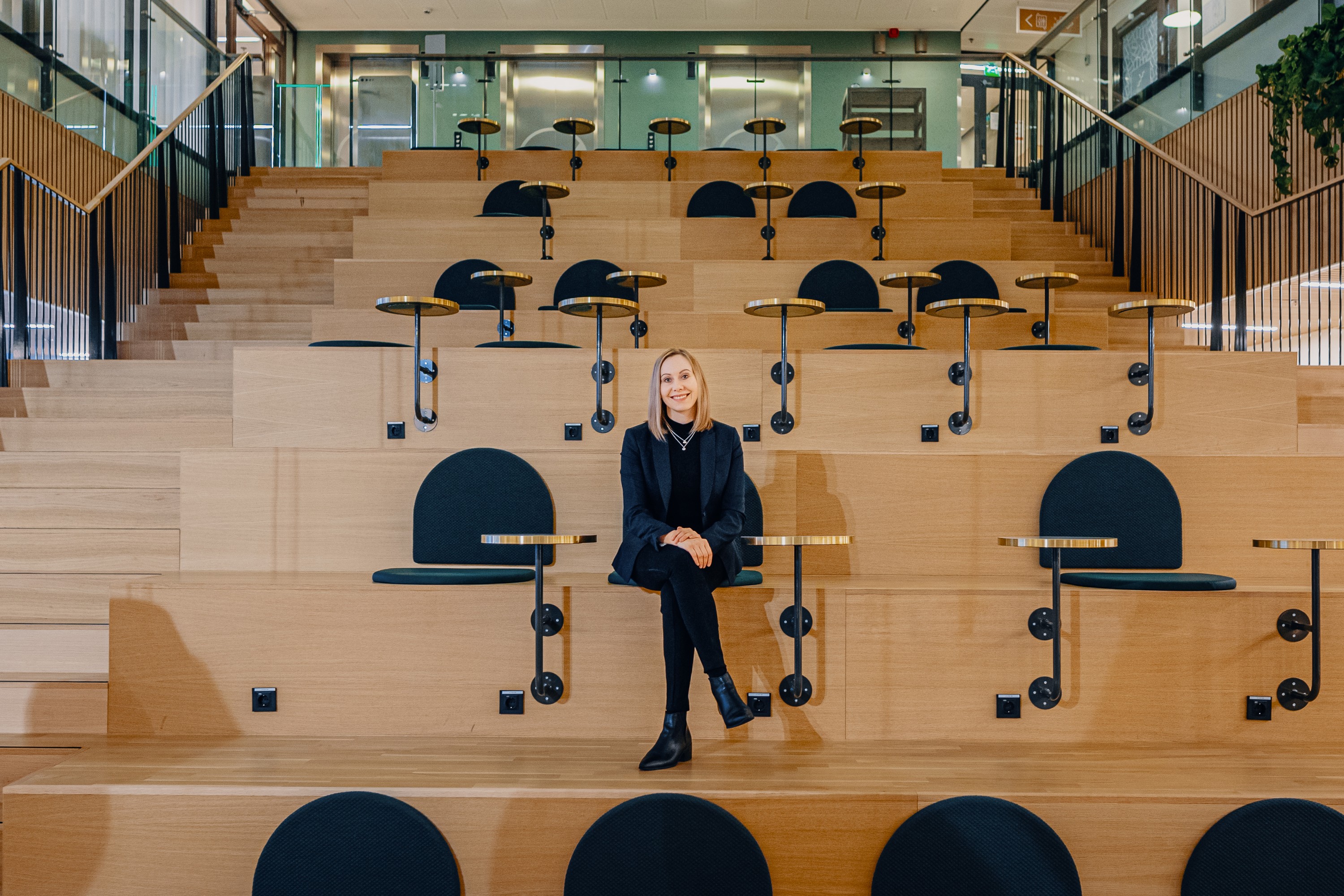 Toimiston atrium, jossa nainen istuu puisilla portailla Nainen istuu yksin toimiston atriumissa puusta tehdyillä istuskeluportailla.