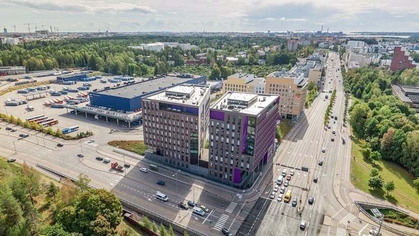 Nykyaikainen Helsingin kaupunkimaisema kaupunkirakennuksineen ja teineen Moderni kaupunkimaisema, jossa on korkeita rakennuksia ja vilkas risteys vehreällä kasvillisuudella.