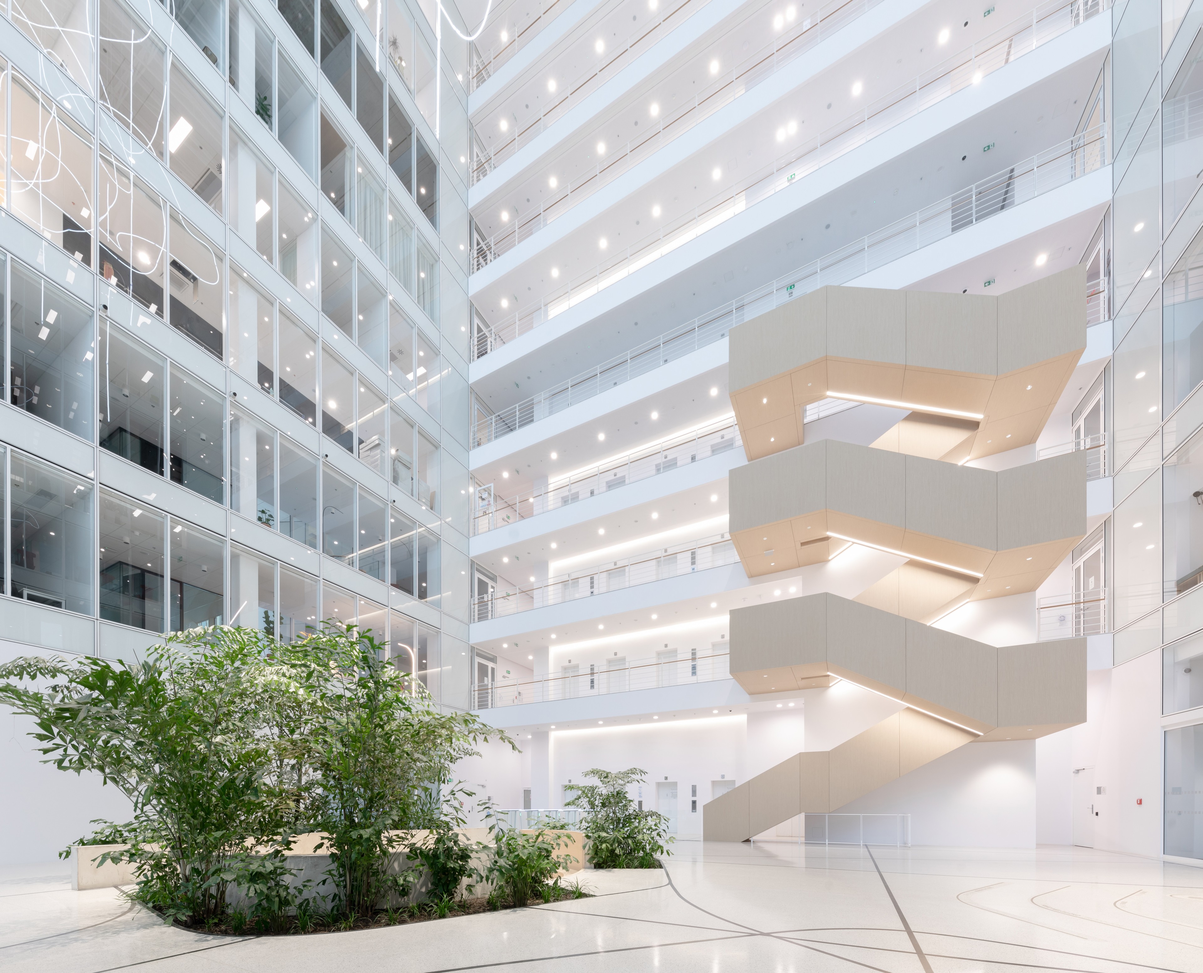 Parkview kancelářská budova Moderní světlé kancelářské atrium se skleněnými stěnami, vnitřními rostlinami a plovoucím schodištěm.