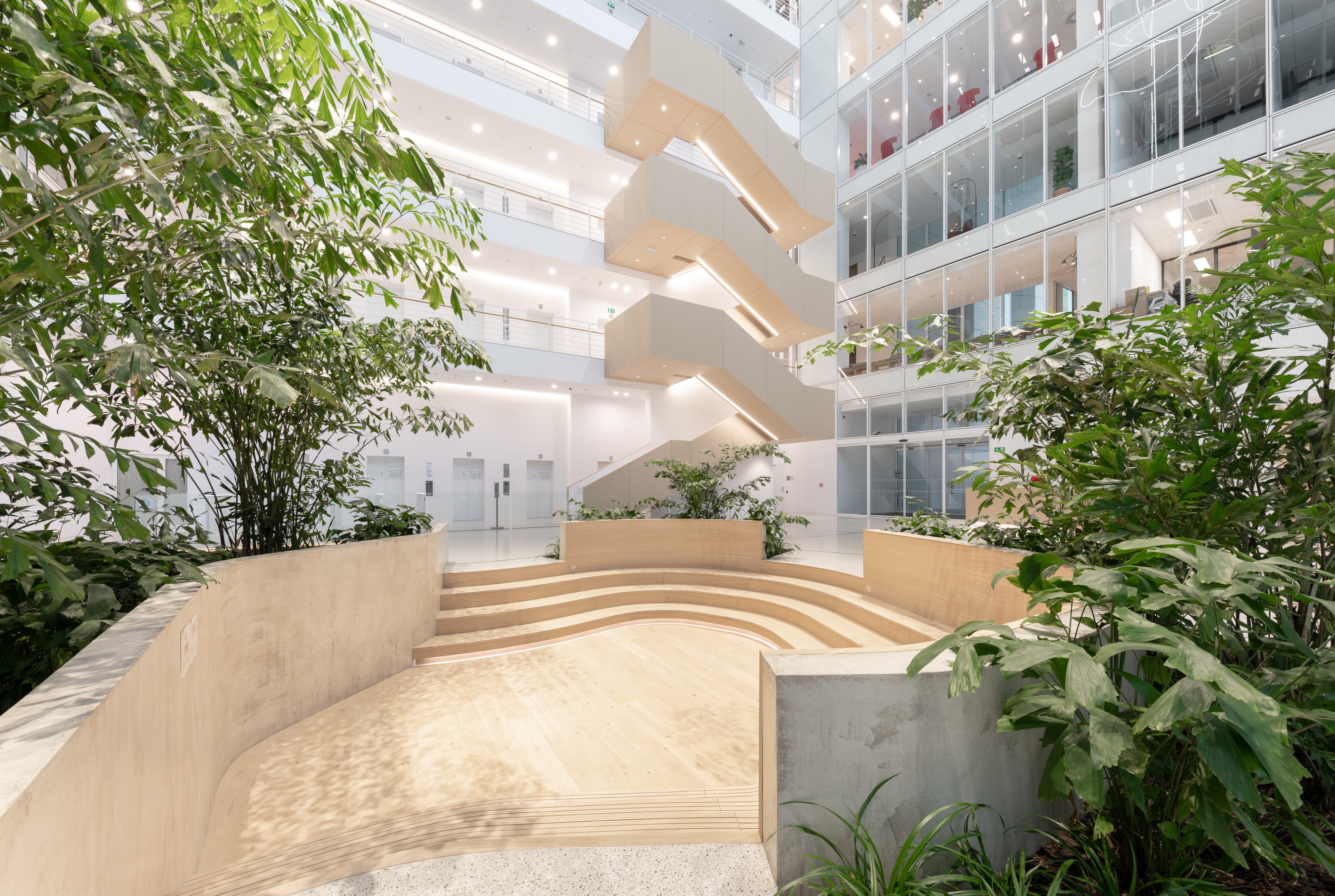 Parkview sunken courtyard Jasné moderní vnitřní atrium se schodišti, skleněnými stěnami a bujnými zelenými rostlinami.