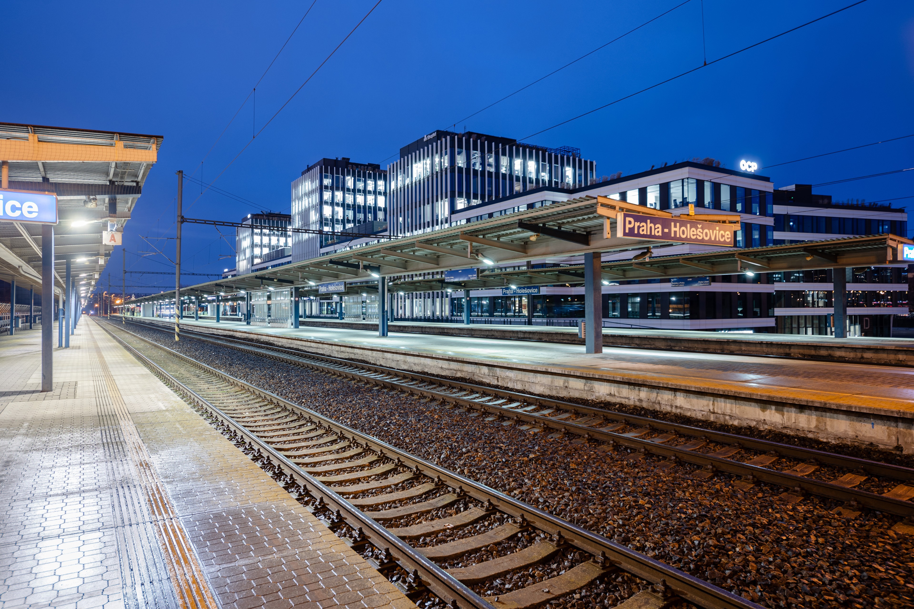 Port7 in the immediate vicinity of Holešovice train and metro station Prague-Holešovice station at dusk with illuminated platforms and modern buildings.