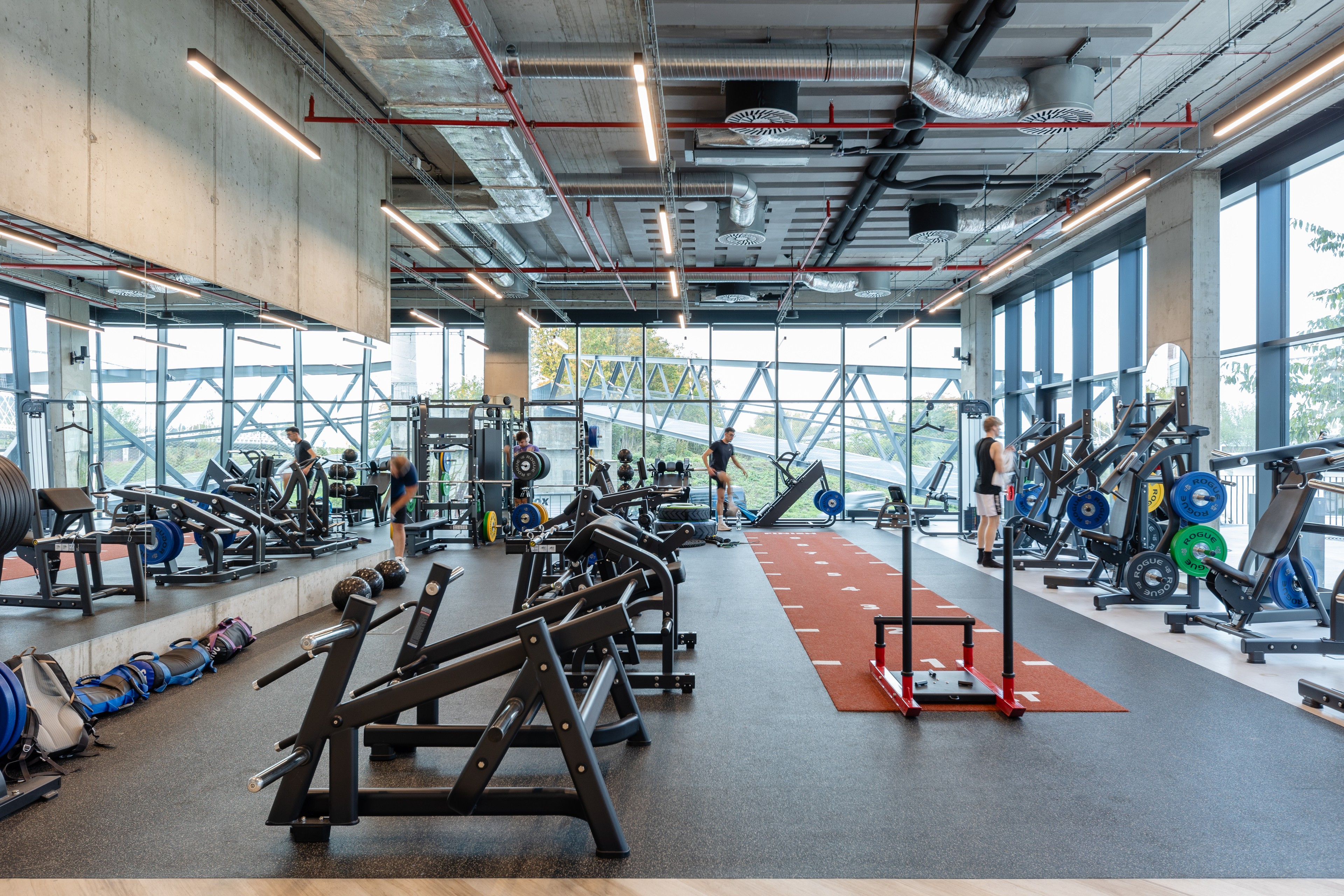 Port7 OneGym fitness center Modern interior of a gym with exercise machines, workout equipment, and large windows.