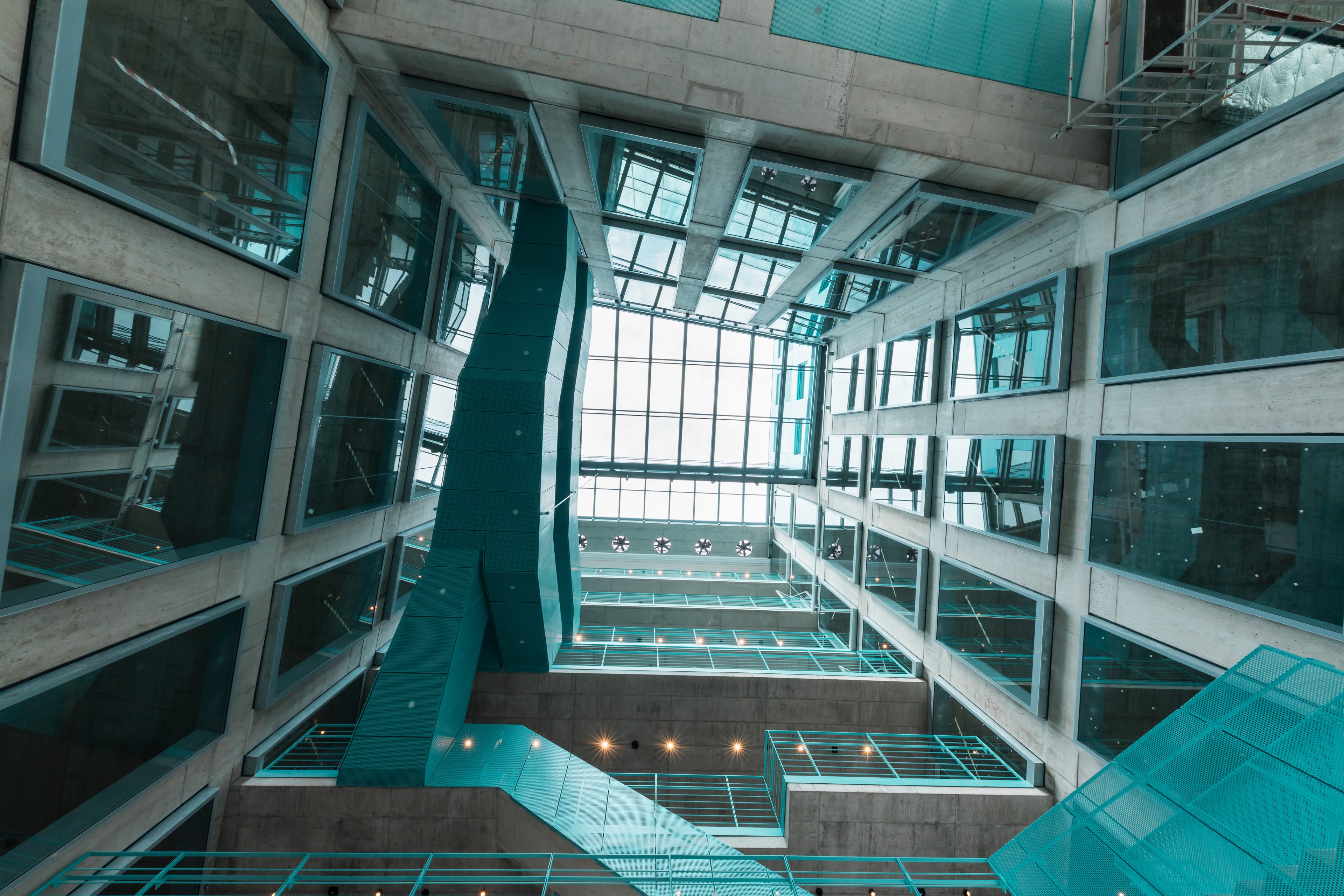 Atrium Praga Studios Interiérový pohled na atrium moderní budovy se skleněnými okny a tyrkysovými schodišti.