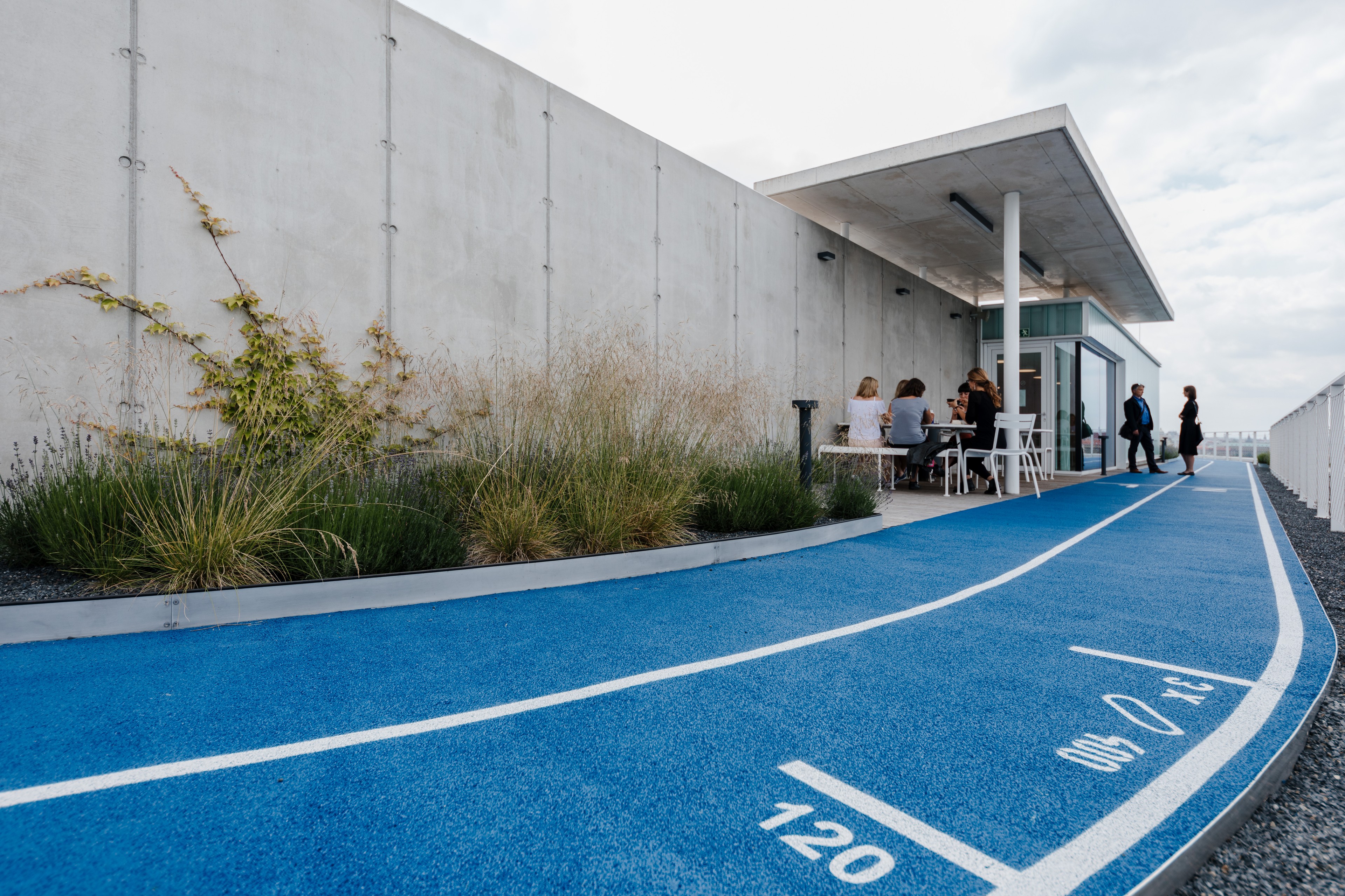 Running track at Visionary Outdoor blue running track next to a modern building with people sitting and walking.