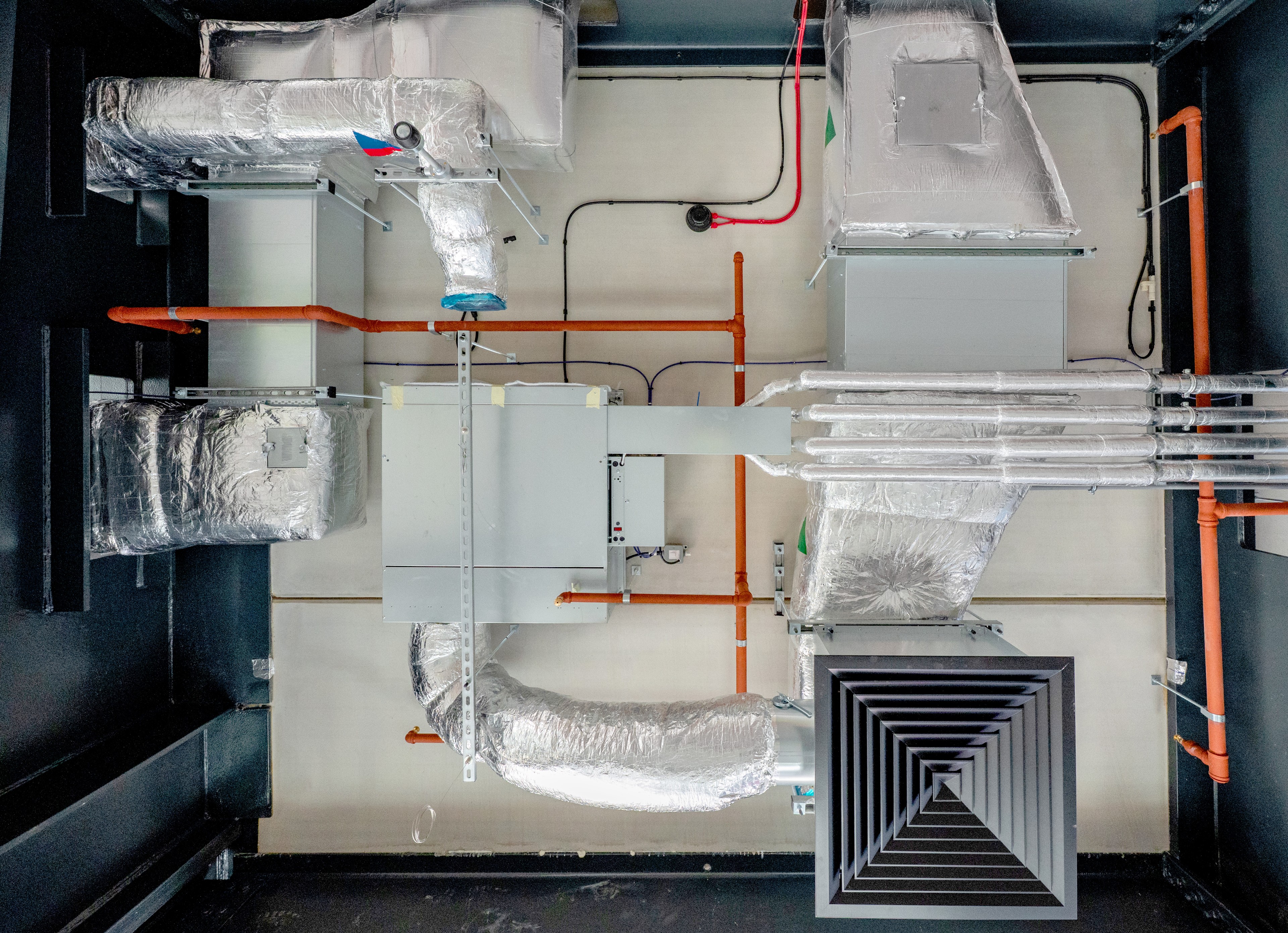 Stropné HVAC potrubie so izolovanými striebornými rúrami a oranžovými komponentmi ventilačného systému.