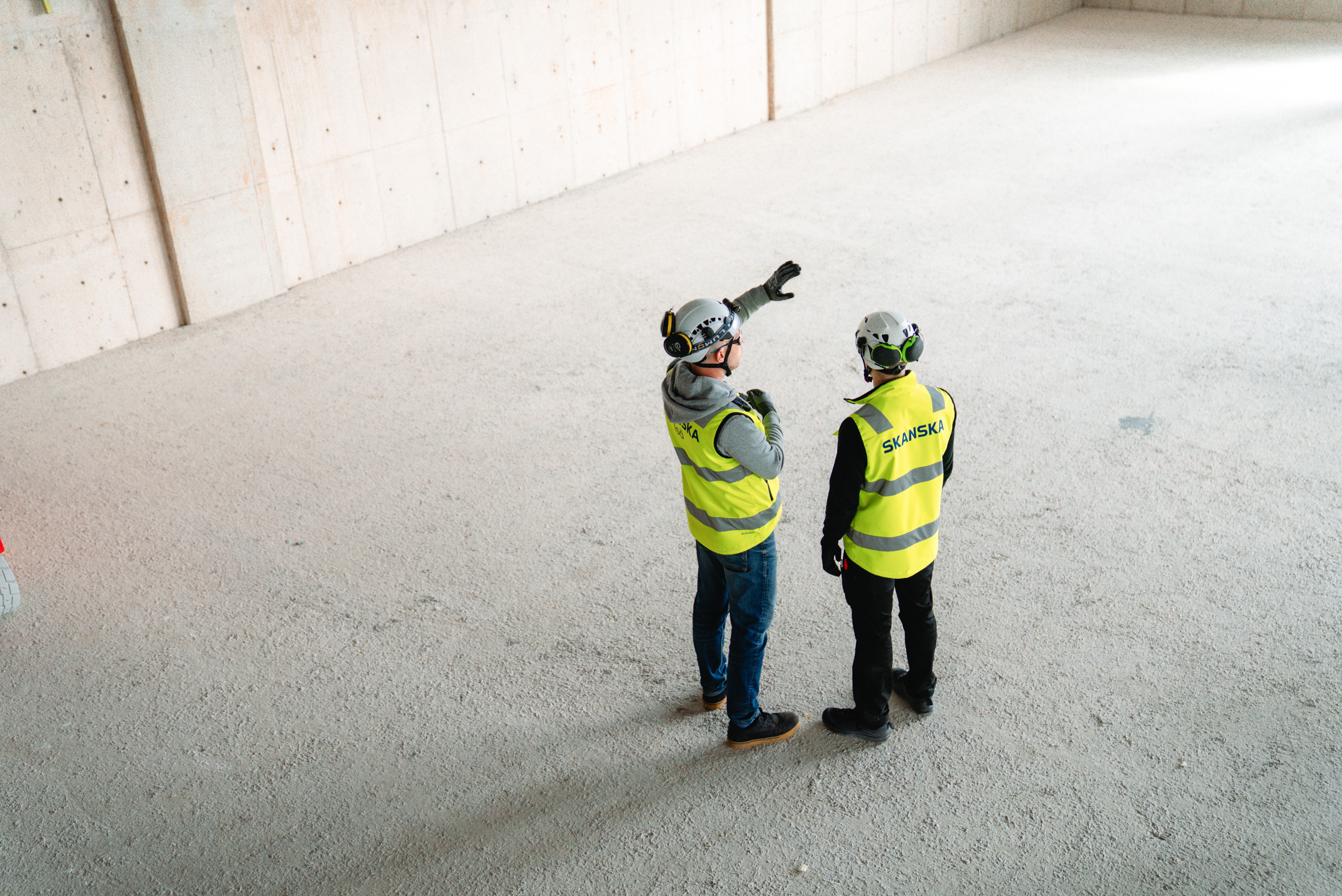 Two construction workers in protective gear discussing plans on an empty construction site.