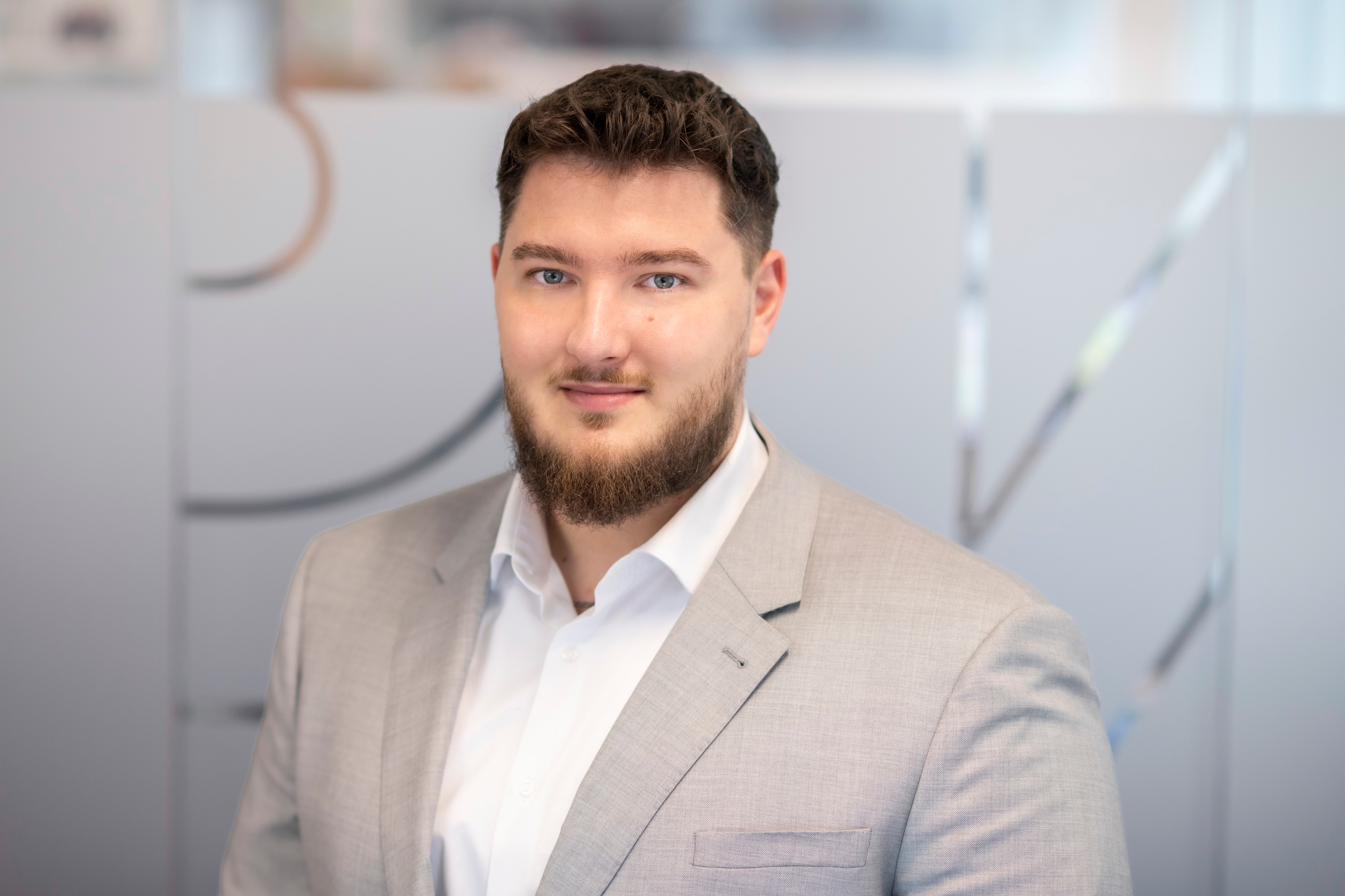 Tomáš Holopírek Profesionální muž v světle šedém obleku a bílé košili stojící v moderní kanceláři.