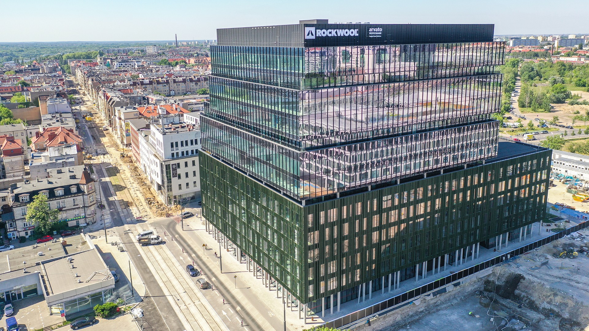 Nowoczesny szklany budynek biurowy z napisem "Rockwool", na tle miejskiego krajobrazu.