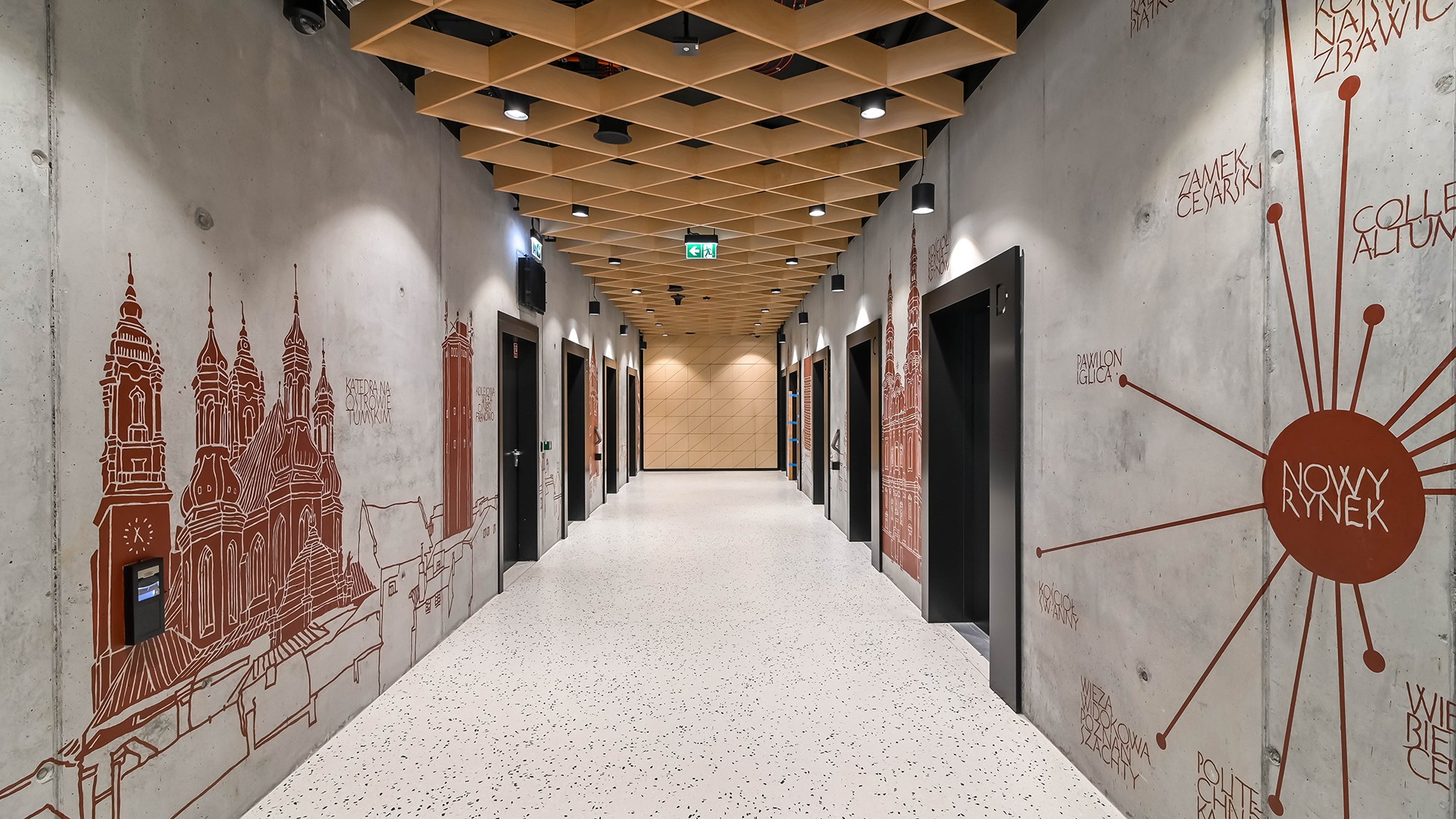 Nowoczesny korytarz z architektoniczną sztuką ścienną, charakteryzujący się geometrycznym designem sufitu i drzwiami windy.