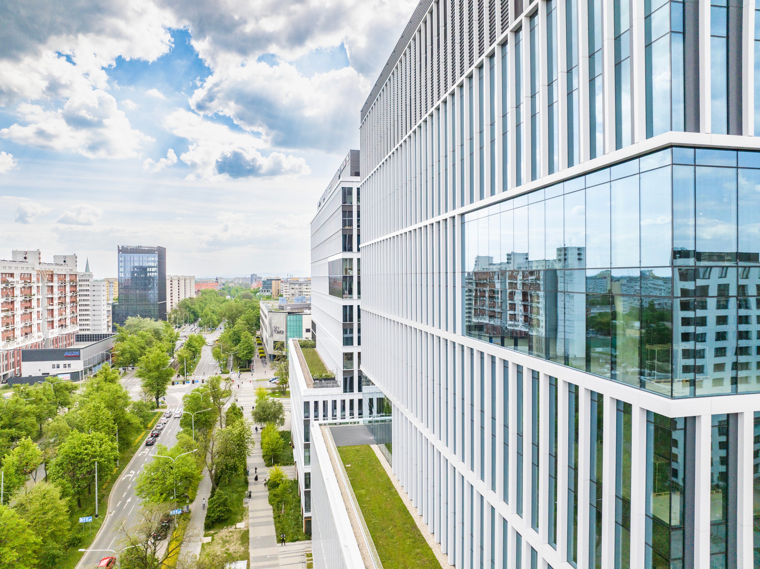 Modern office building with reflective glass windows overlooking a tree-lined city street.