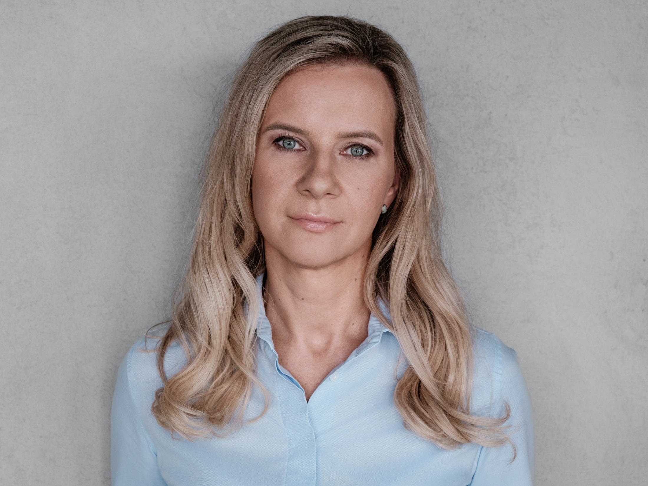 Professional woman with long blonde hair in a light blue shirt Blonde woman with long wavy hair in a light blue shirt on a gray background.