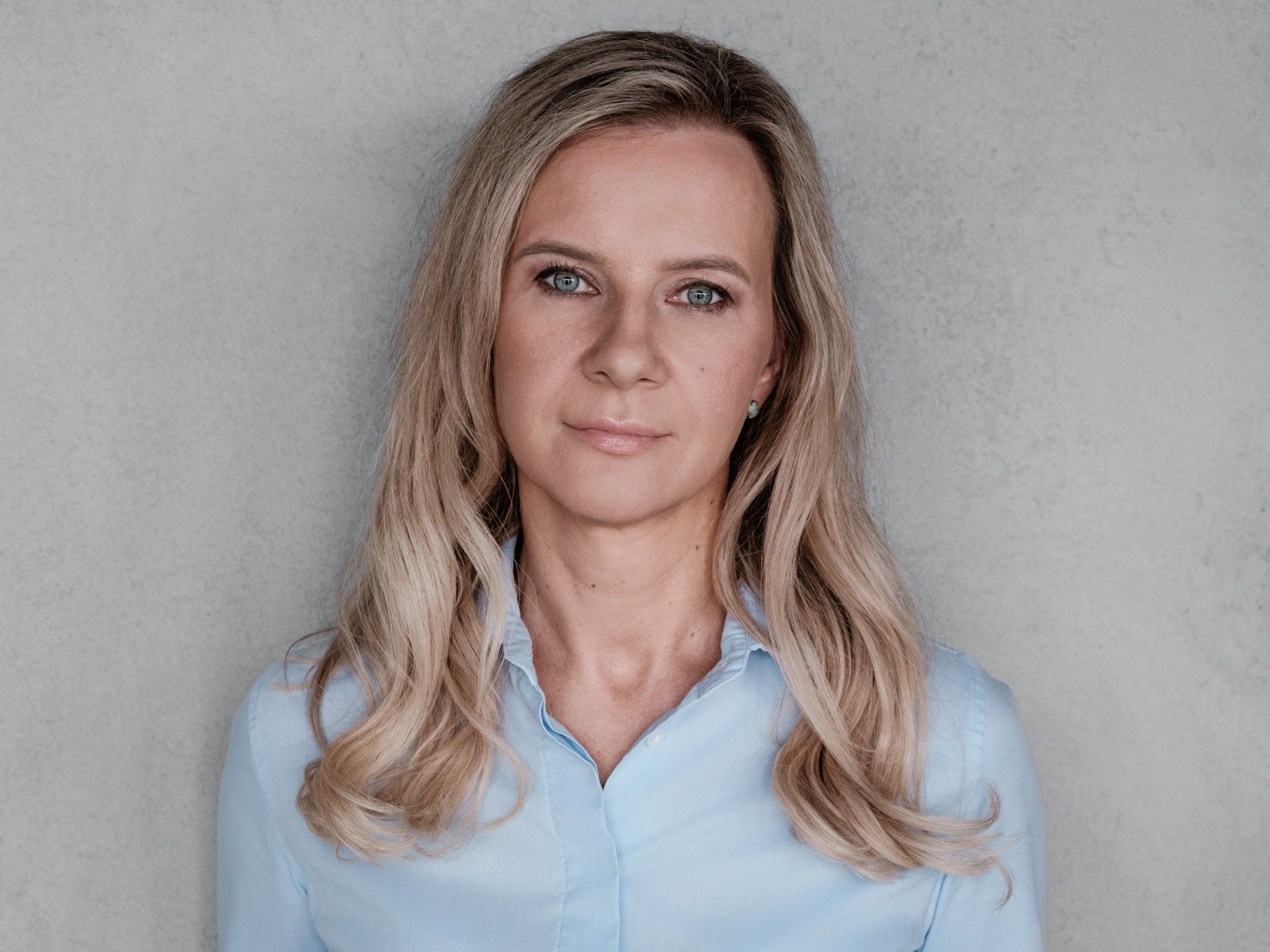Professional woman with long blonde hair in a light blue shirt Blonde woman with long wavy hair in a light blue shirt on a gray background.