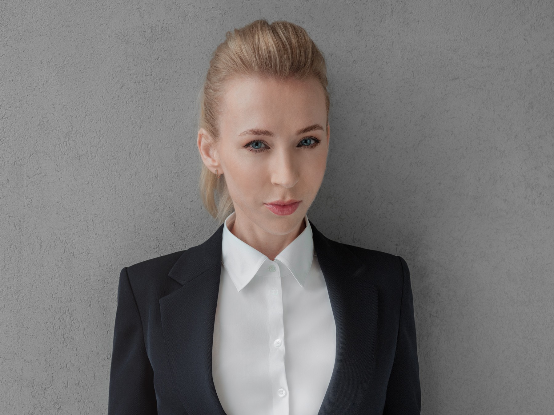 Professional businesswoman in a black jacket and white shirt A professional woman in a black blazer and white shirt standing against a gray wall.