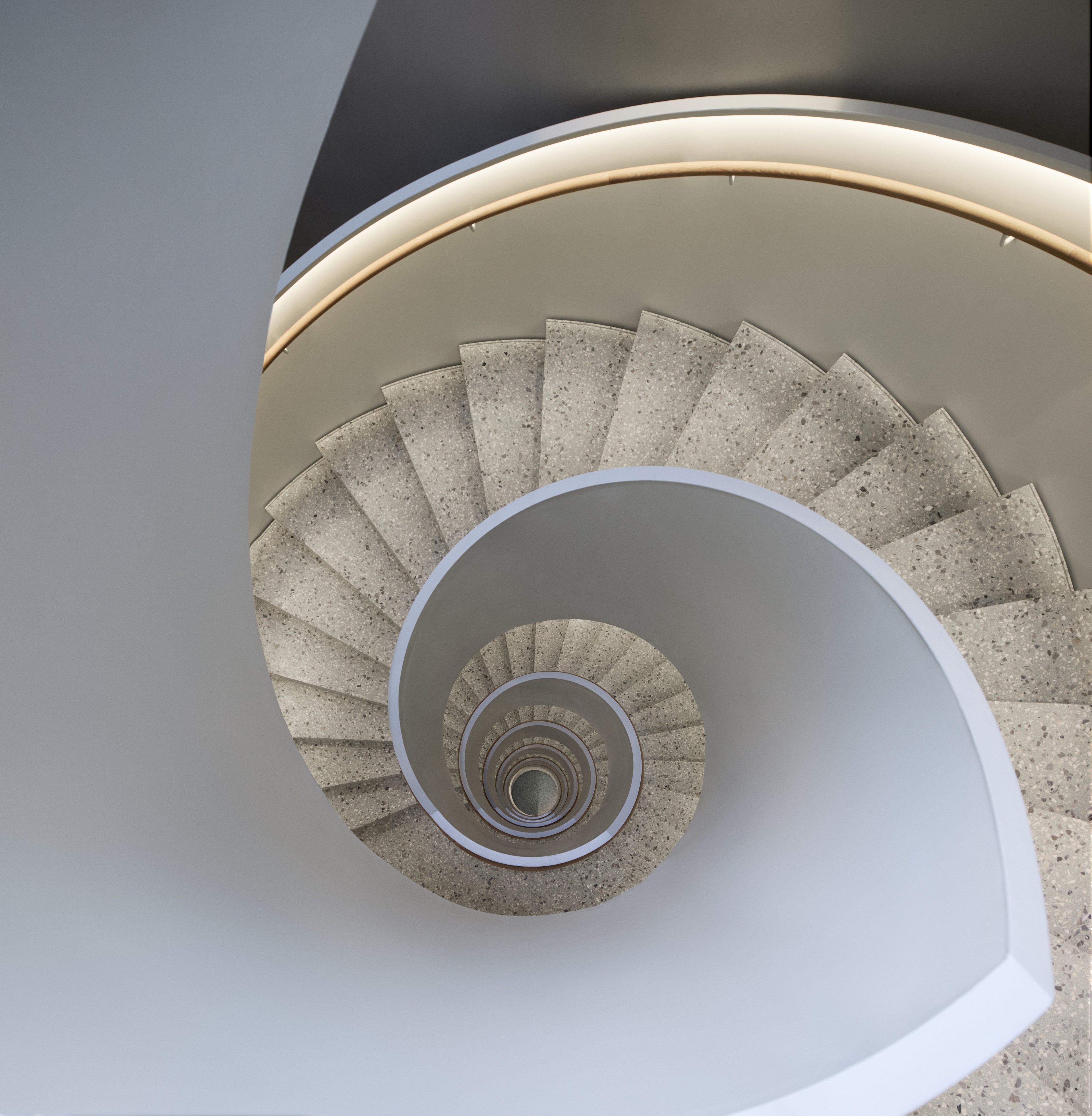 Spiraltrappa med stentrappsteg och modernt vitt böjt räcke sedd ovanifrån.