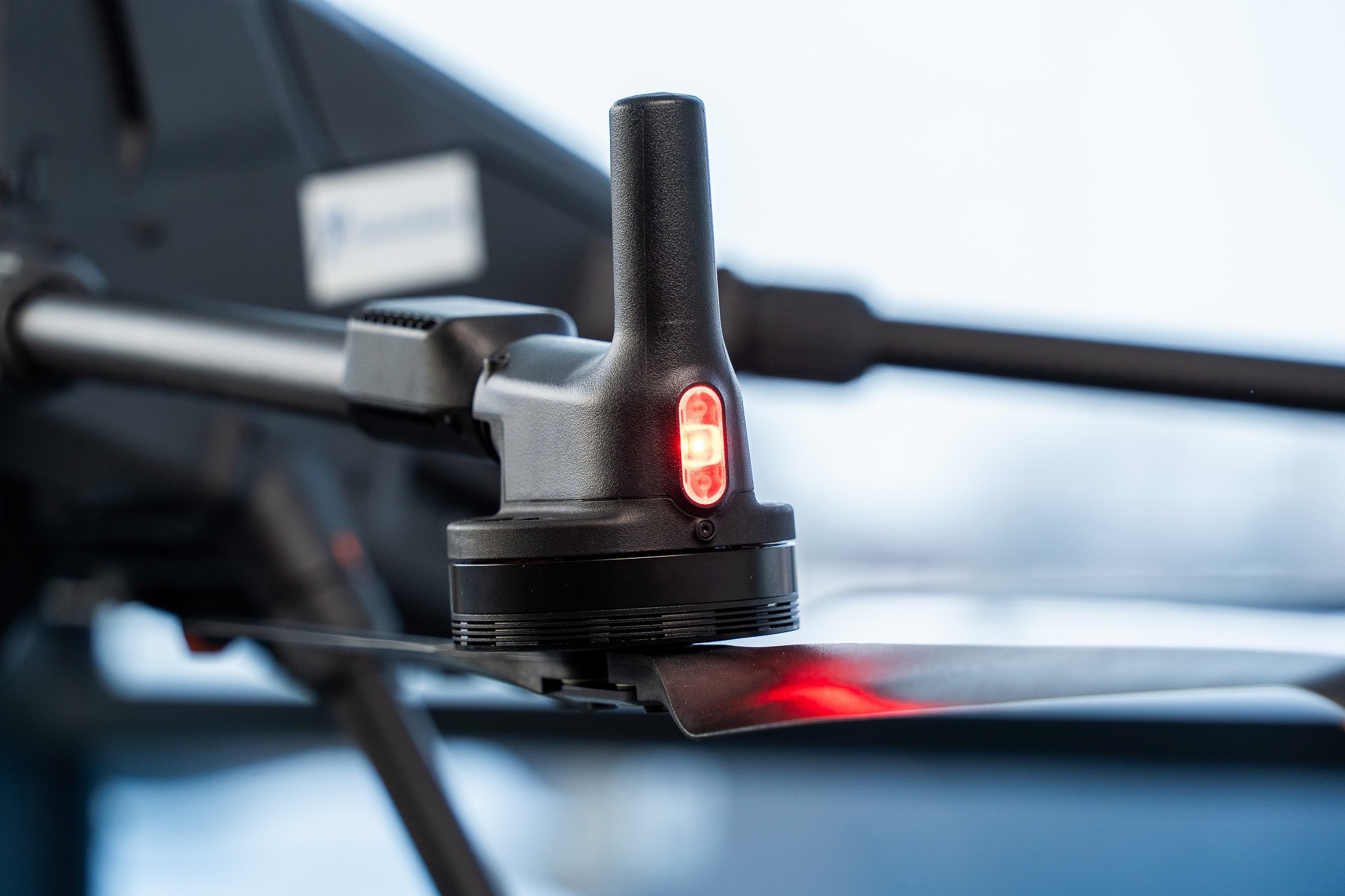 Detailní záběr motoru vrtule dronu s červenou kontrolkou na rozostřeném pozadí.