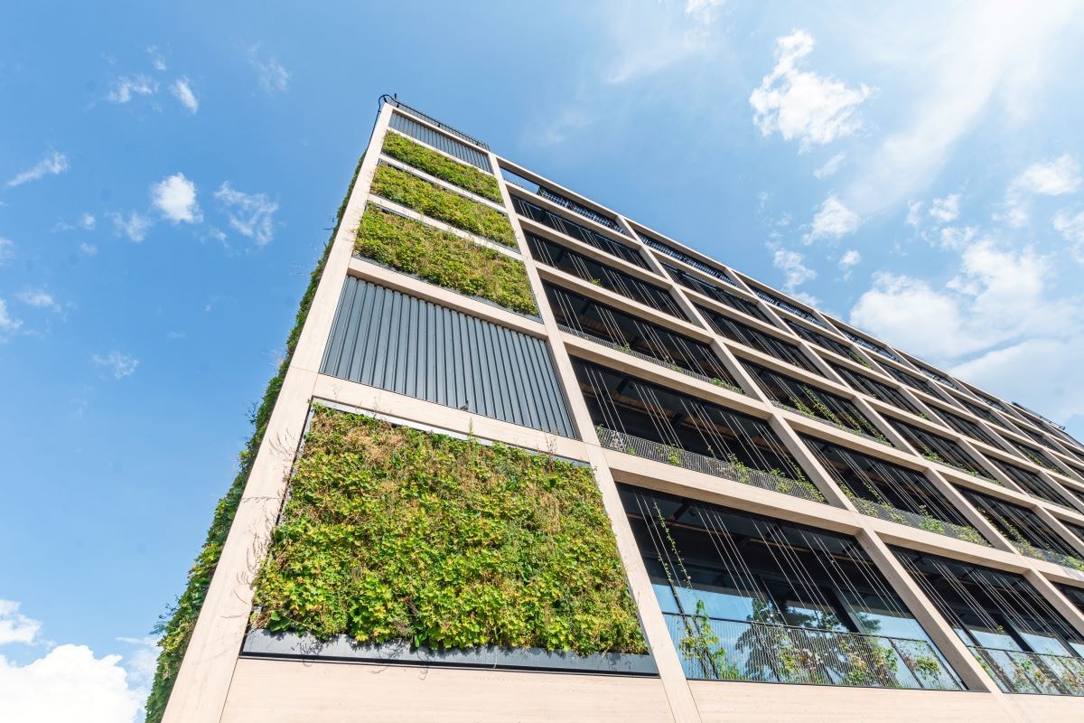 Modern building with vertical garden walls under blue sky Nowoczesny budynek z pionowymi zielonymi ścianami pod czystym niebieskim niebem, prezentujący zrównoważony design.