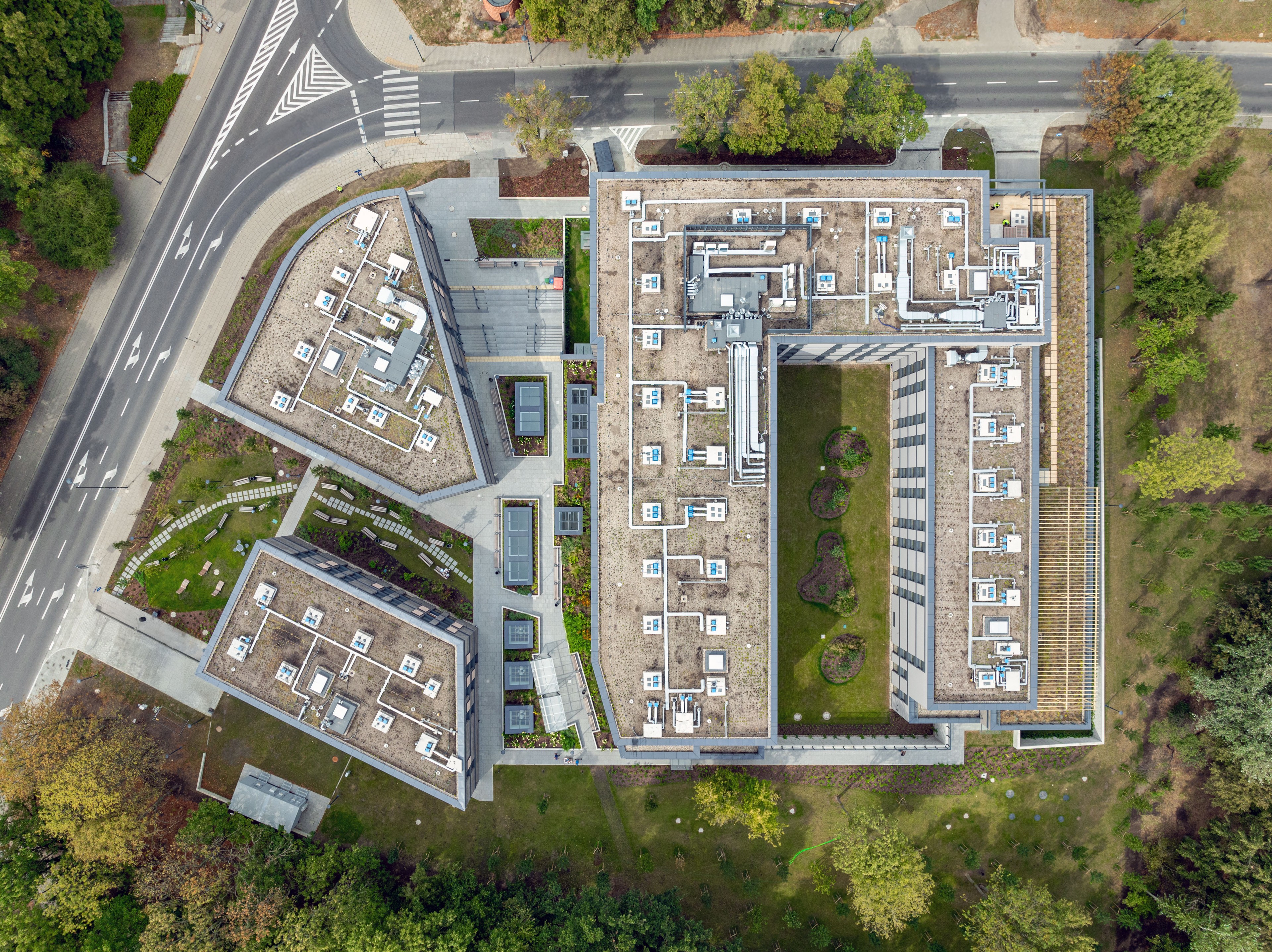 Aerial view of modern office buildings with green surroundings Widok z lotu ptaka na nowoczesne miejskie budynki z jednostkami HVAC na dachach i zielonym zagospodarowaniem terenu.