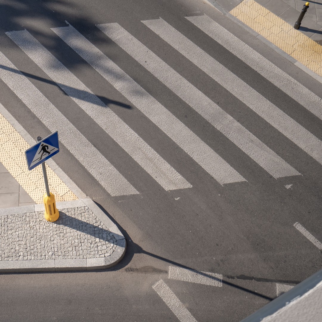 Widok z lotu ptaka na przejście dla pieszych z niebieskim znakiem przejścia, otoczone teksturowaną nawierzchnią.