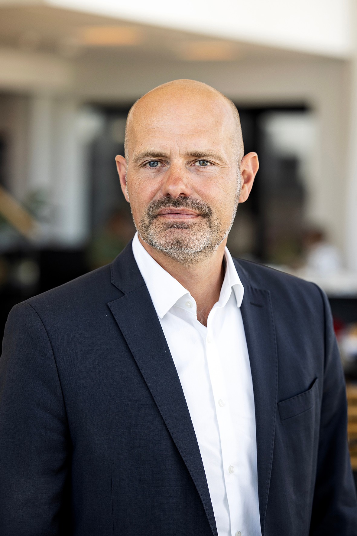Peter Nymann Professionell man i en marinblå kostym och vit skjorta i en modern kontorsmiljö.