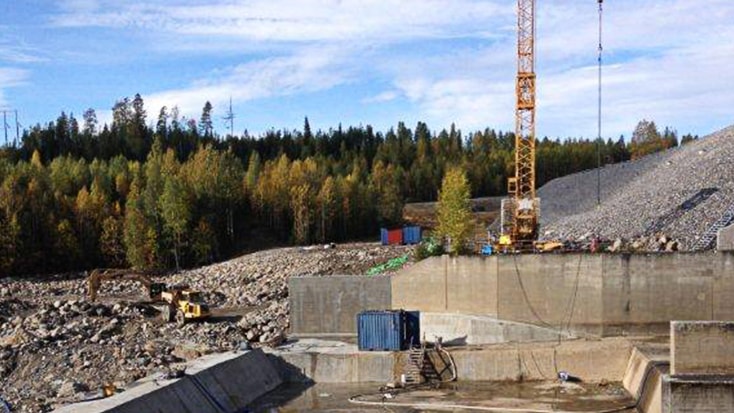 Betongarbetena färdigställda. Till vänster syns den nya, tre meter höga, energiomvandlaren. Byggarbetsplats med kran, fraktcontainer och grävmaskiner bland klippig terräng.