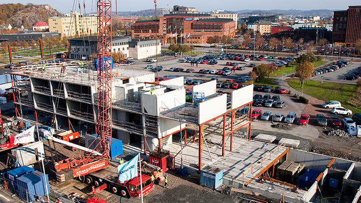 Det har varit en snabb och effektiv byggprocess. Byggarbetsplats med kranar som monterar prefabricerade betongstrukturer nära en parkeringsplats.