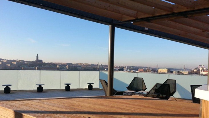 Hotellet har en fantastisk utsikt över hamninloppet. Takterrass med moderna sittplatser och panoramautsikt över staden under en klarblå himmel.