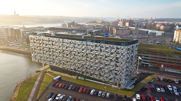 Radison Blu Riverside Hotel. Modernt hotell med geometrisk fasad vid vattenfronten, omgiven av stadsbild och parkerade bilar.