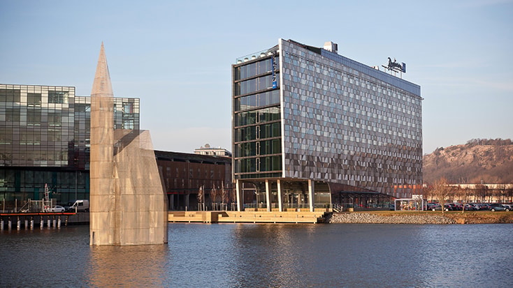 Radisson Blu Riverside Hotel ut över en av hamnbassängerna. Modern byggnad vid vattnet med en geometrisk skulptur i ett rofyllt stadsmiljö.