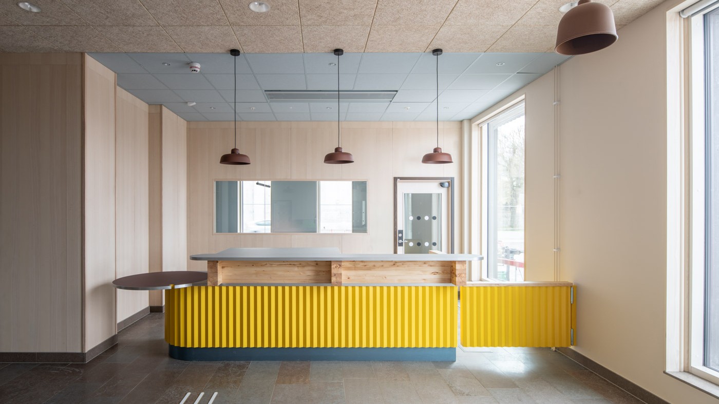 Interiören är ljus och modern. Foto: Anders Bobert Interiörbild av en köksdisk med gult ribbat trä, träpaneler och hängande lampor i modern stil.
