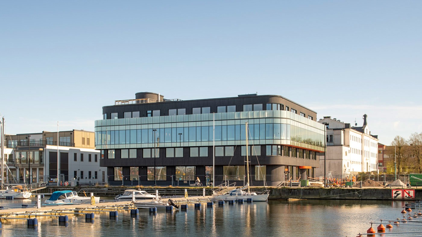 Kontoret på 4 900 kvadratmeter ligger på Skeppsbrokajen och blir en signaturbyggnad Utsikt mot en Boverkets huvudkontor med svarta och glasade fasader vid en marina med båtar.
