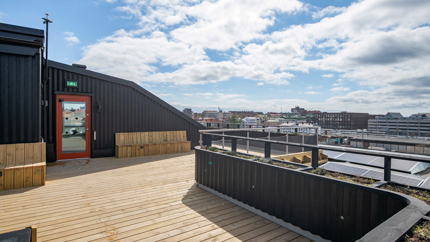 Takterassen bjuder på en utsikt över staden. Foto: Anders Bobert Takterrass med trädäck, bänkar och vy över en stad med solpaneler i förgrunden.