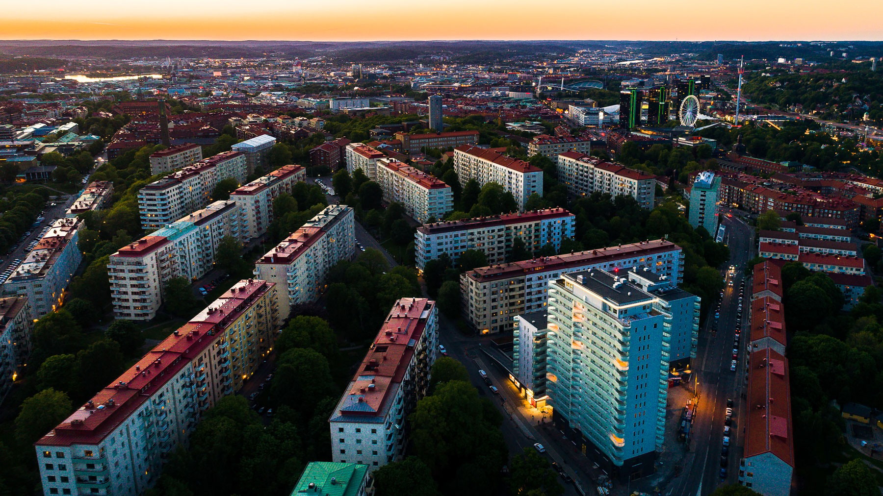 Flygvy över Göteborgs stadsbild vid solnedgången, som visar bostadsbyggnader och ett pariserhjul.