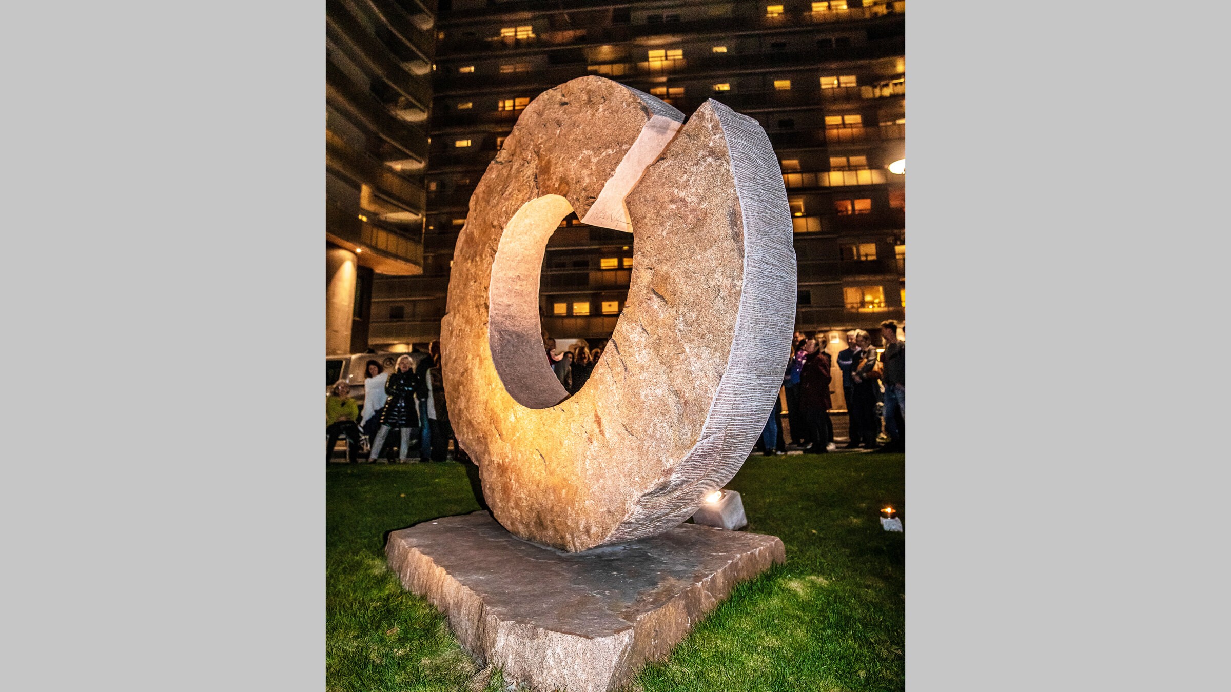 Upplyst stenskulptur som liknar en stor cirkulär ring, visad utomhus på natten.