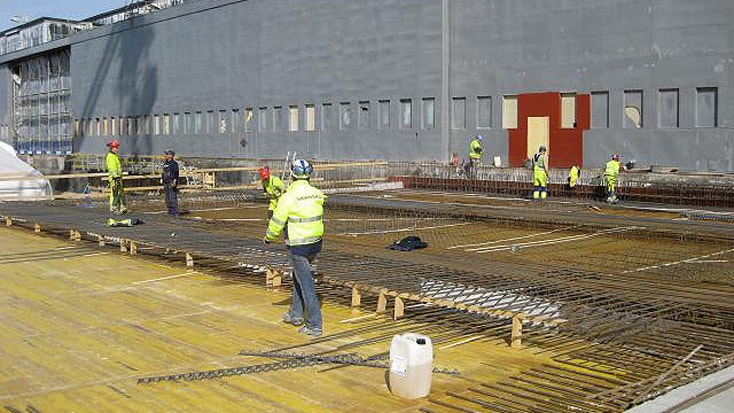 Byggnadsarbetare installerar armeringsjärn på en stor byggarbetsplats, förbereder för betonggrundsarbete.