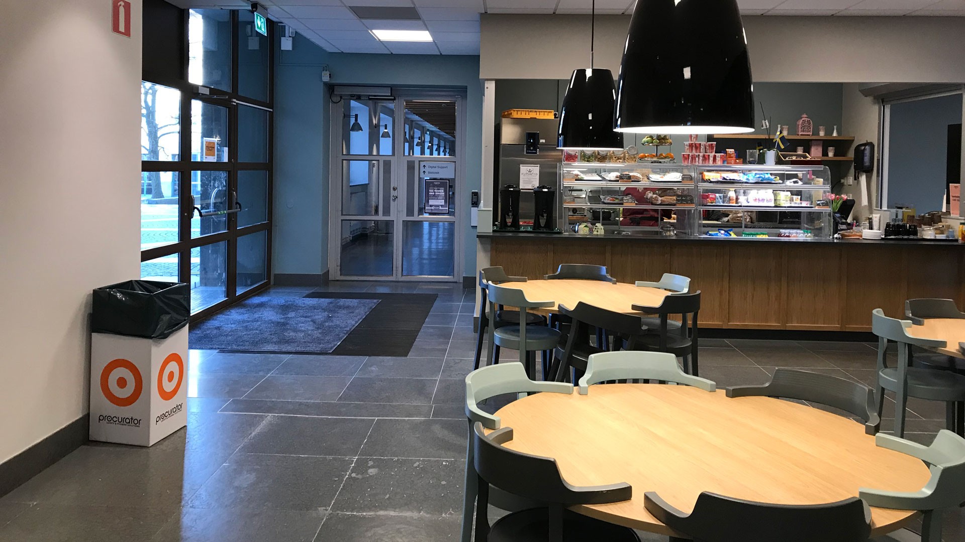 Modern kaféinteriör med runda bord, stilfull belysning och en disk som visar olika snacks.