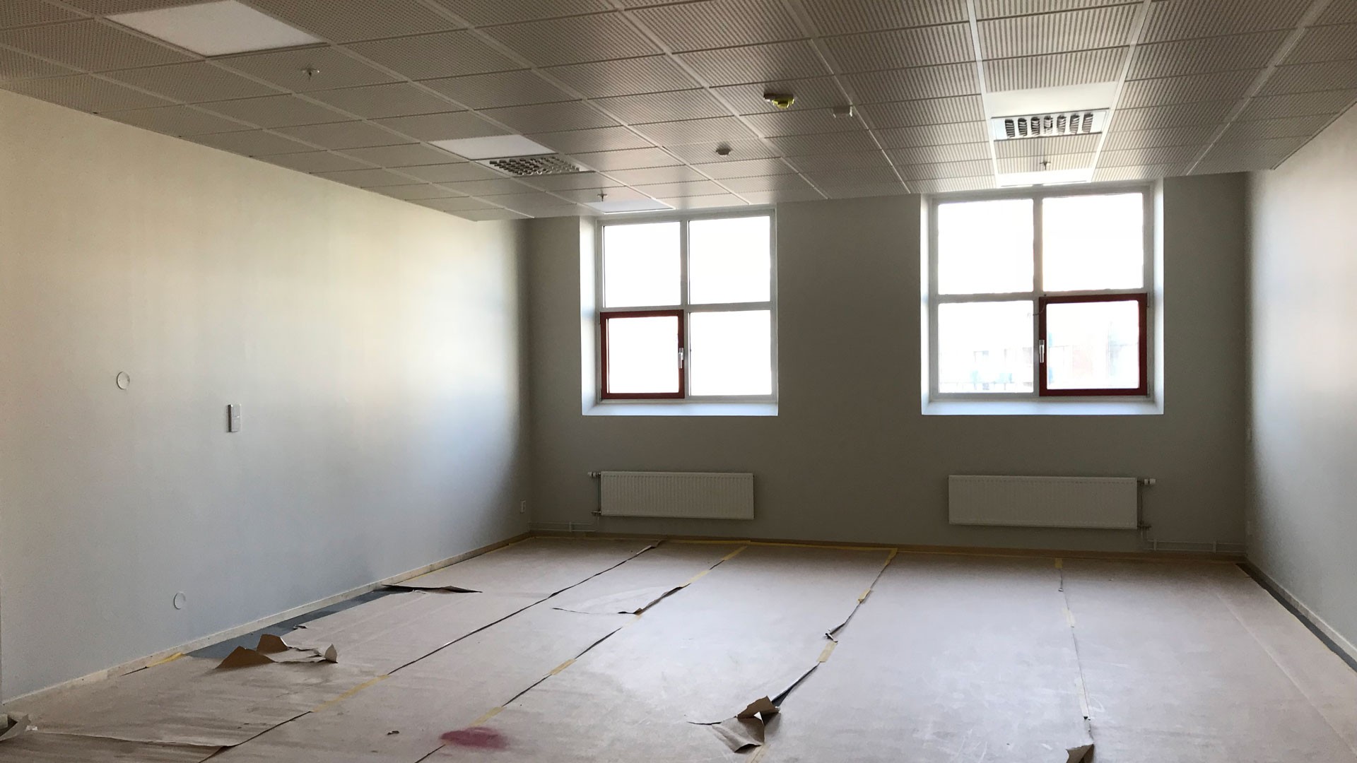 Tomt rum med stora fönster, kaklat tak och radiatorer, med golv täckt för renovering.