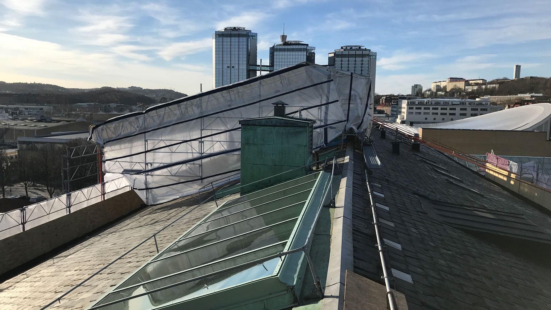 Takterrassutsikt med en delvis kollapsad struktur och stadssilhuett i bakgrunden.
