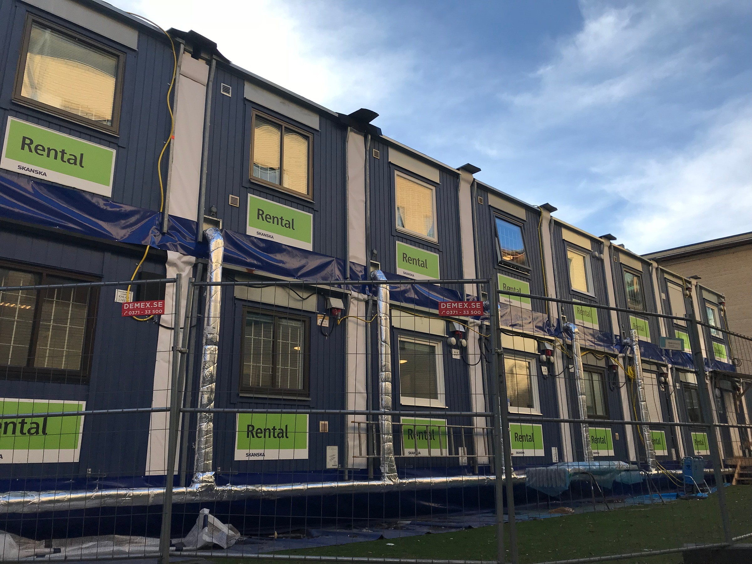Tvåvånings modulära hyresenheter med "Rental"-skyltar, omgivna av ett byggstängsel.