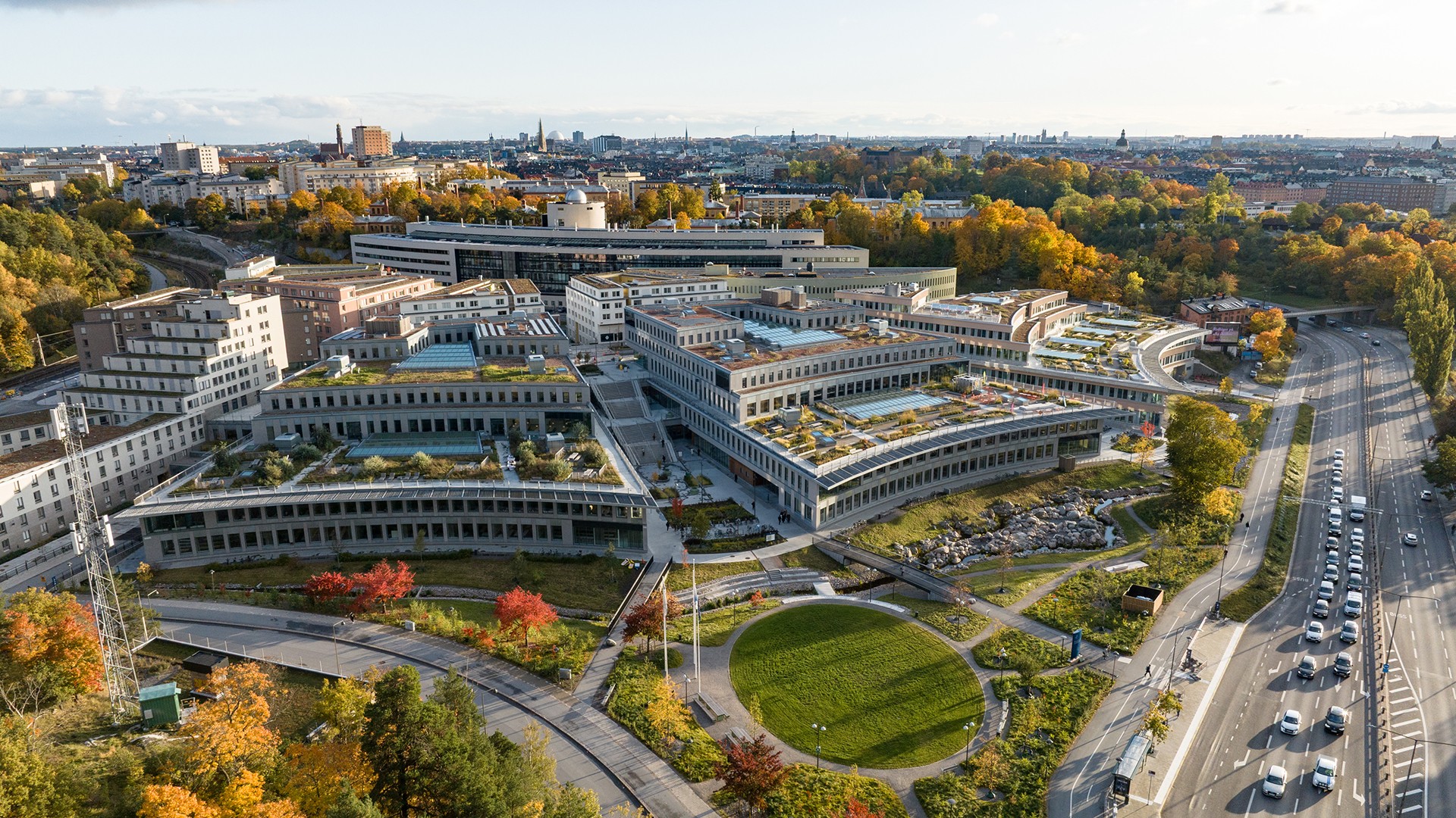 Campus Albano – en ny samlingspunkt för Stockholms studenter. I samverkan med Akademiska Hus skapade vi 65 000 kvm utbildningslokaler med fokus på lärande, hållbarhet och biologisk mångfald. Foto Anders Bobert Drönarvy över campusbyggnader och gröna ytor med intilliggande vägar.