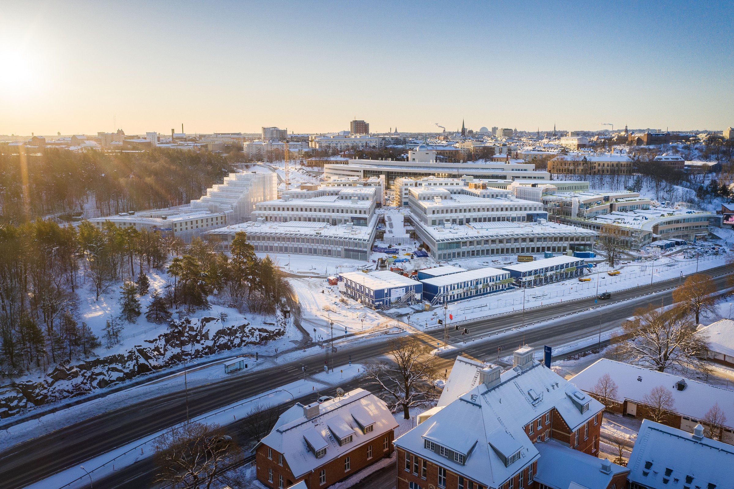Flygvy över ett snöigt stadslandskap med moderna byggnader och solbelysta vägar.
