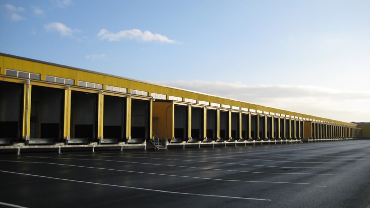DHL Gult lager med flera lastbryggor och en stor, tom parkeringsplats under en klar himmel.