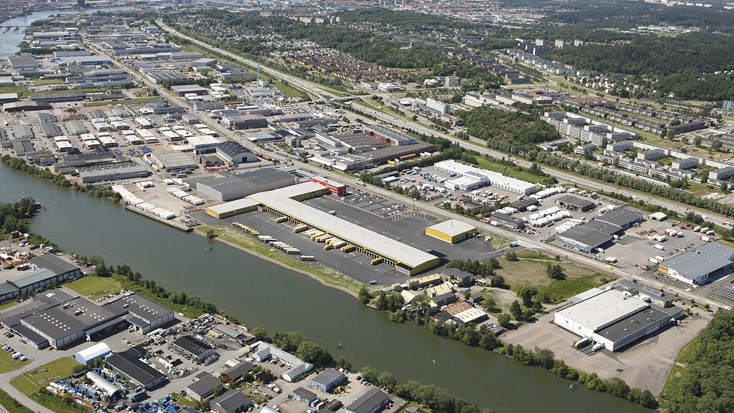 DHL Flygvy över ett industriområde bredvid en kanal, med lager och vägar i en vidsträckt layout.