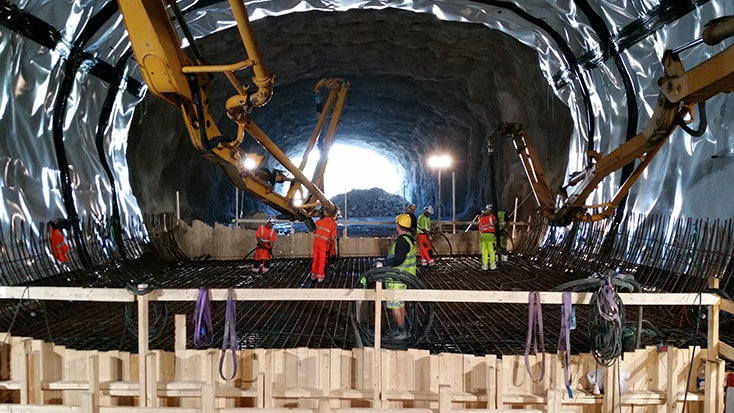 Byggnadsarbetare och maskineri inne i en delvis byggd tunnel med förstärkt stål.