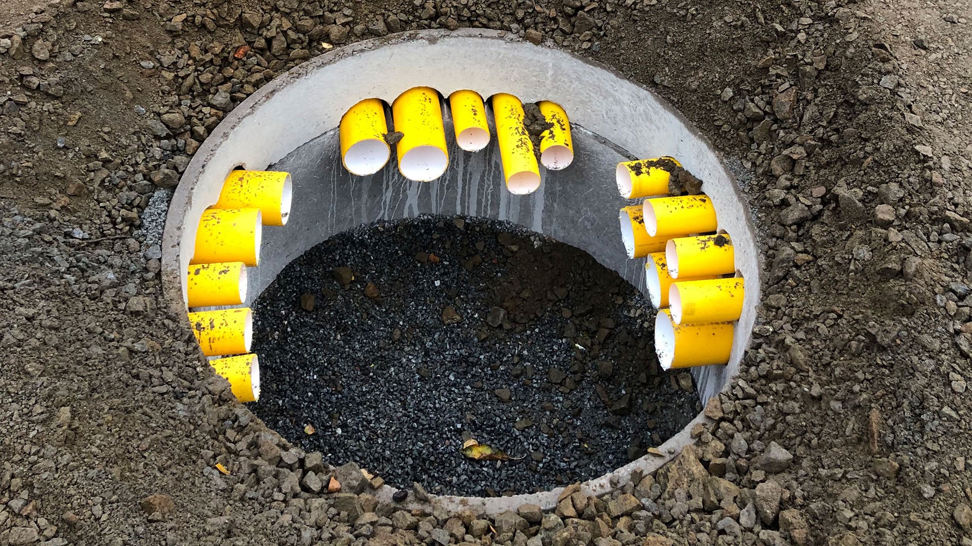 Arbetet utgör en viktig del av infrastrukturen för framtidens eldrivna bussflotta. Nedgrävd kabelbrunn med gula kabelrör som en del av Skanskas elektrifieringsprojekt för elbussar vid Gubbängens och Nybodas bussdepåer.
