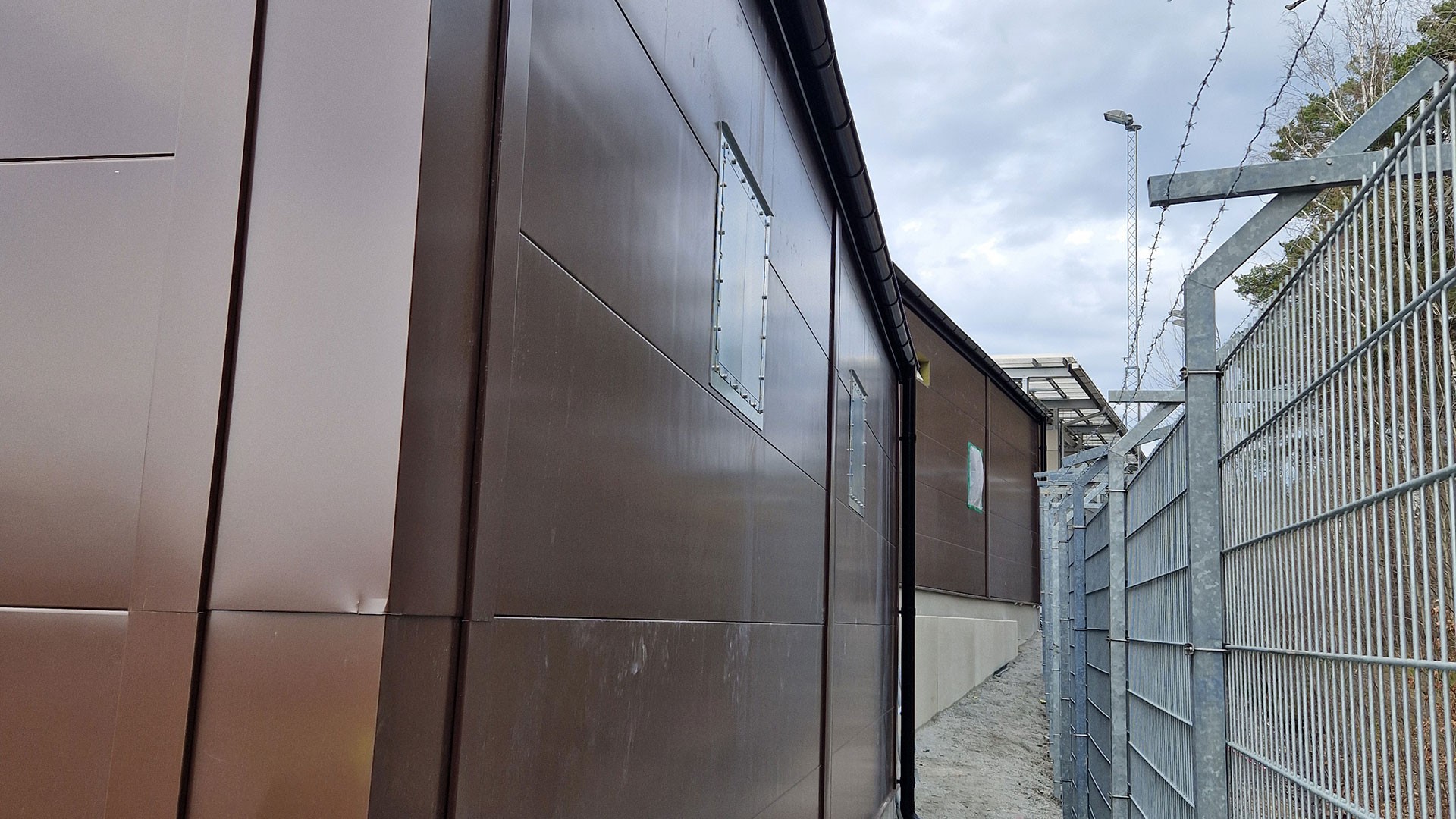 Skanskas arbete möjliggör laddning av över 120 elbussar och bidrar till Stockholms klimatomställning. Brun fasad på ett av de teknikhus som byggts vid Gubbängens och Nybodas bussdepåer inom Skanskas elektrifieringsprojekt för elbussar i Stockholm.