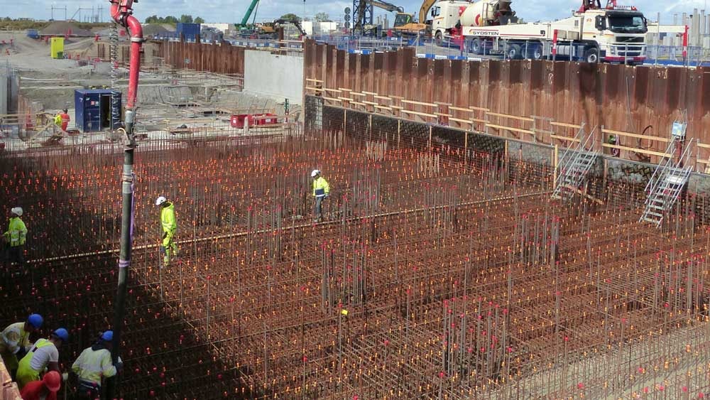 Byggnadsarbetare på plats med omfattande armeringsjärnsinstallation, förbereder för betonggjutning.