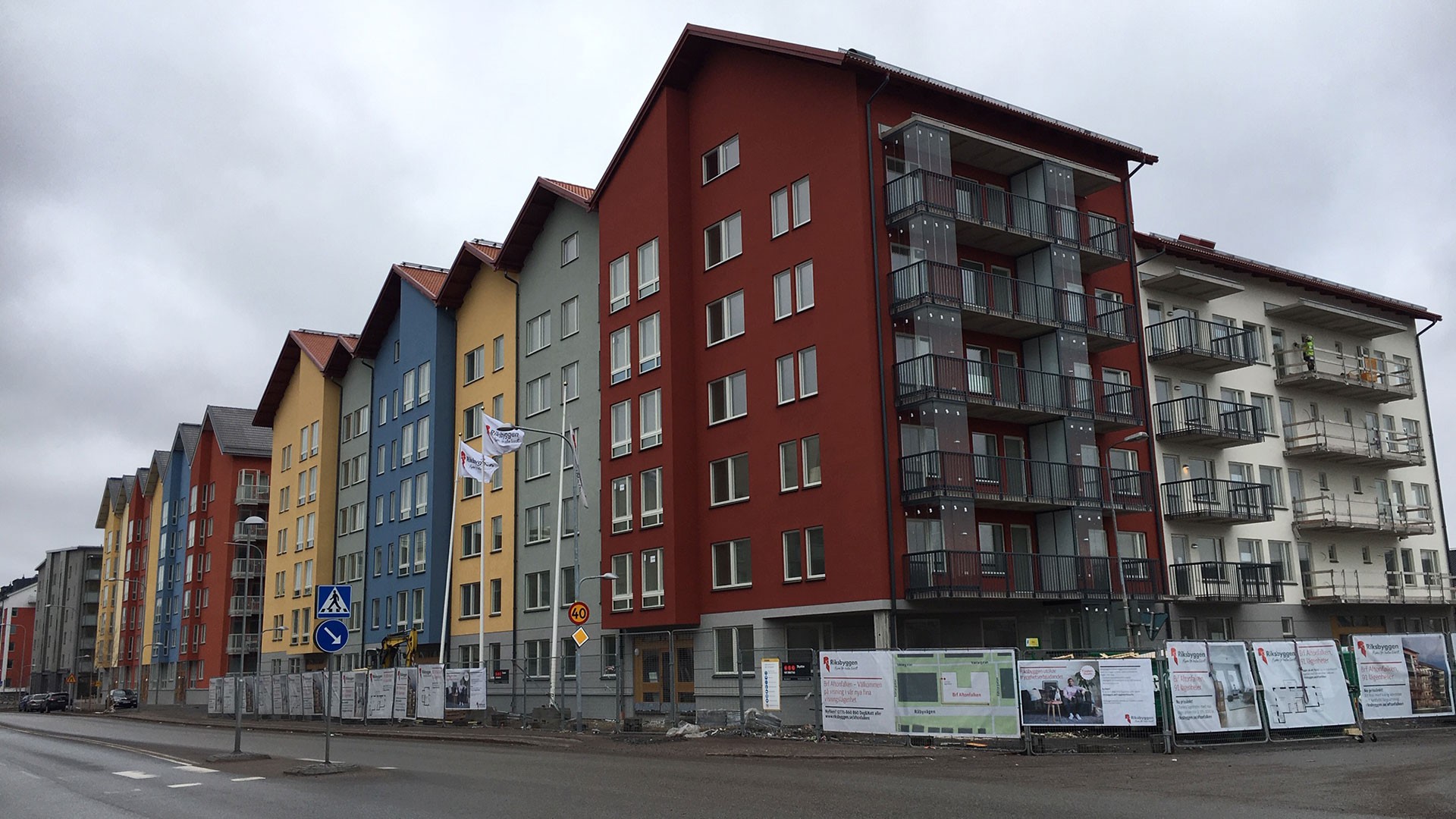 Färgglada moderna lägenhetsbyggnader med sadeltak kantar en gata under en molnig himmel.